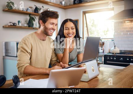 Glücklicher junger Kaukasier, der an einem Laptop arbeitet, während seine Frau neben ihm steht und sie zusammen auf den Bildschirm schauen. Ein Mann, der freiberuflich arbeitet und Showin Stockfoto