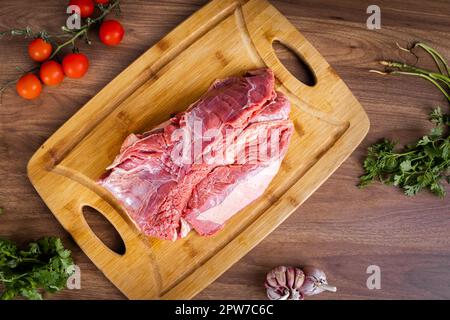 FLANK STEAK Beef BBQ Essen. Mit Fett bedecktes rohes Fleisch auf einem Holzbrett auf einem Holzhintergrund. Gewürzt mit Koriander, Knoblauch und Tomaten. Stockfoto