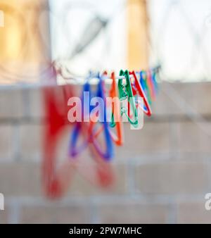 Nahaufnahme einer Gruppe von bunten Klamotten an einer Wäscheleine draußen während des Tages. Plastikstifte zum Aufhängen von Wäsche und Wäsche zum Trocknen als Teil Stockfoto