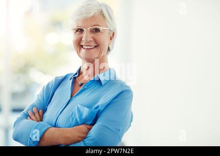 Selbstvertrauen wächst mit dem Alter. Verkürztes Porträt einer älteren Frau, die zu Hause mit gefalteten Armen steht. Stockfoto