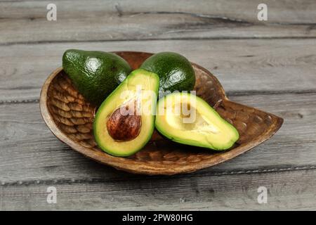 Avocados in Holz geschnitzte Schale, eine davon halbiert, Samen sichtbar. Stockfoto