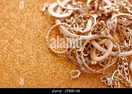 Viele teure goldene Schmuckringe, Ohrringe und Halsketten auf goldenem Glitzerhintergrund mit glänzenden Funkeln. Pfandhaus oder Schmuckgeschäft Konzept Stockfoto