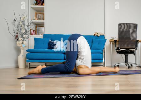 Junge Frau praktiziert Yoga zu Hause, tun Pflug Pose Stockfoto