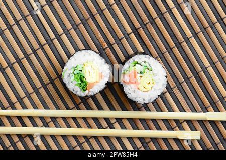 Sushi rollen und liegen auf einem hölzernen Eßstäbchen Bambus Stroh serwing Mat. Traditionelle asiatische Lebensmittel. Ansicht von oben. Flach Minimalismus shot mit kopieren. Stockfoto