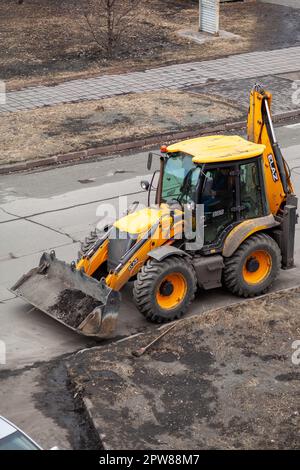 26.04.2023, Kemerovo, Russland. Ein gelber Traktor steht oder fährt auf der Straße bei Straßenarbeiten. Straßenreinigung mit einem Traktor Stockfoto