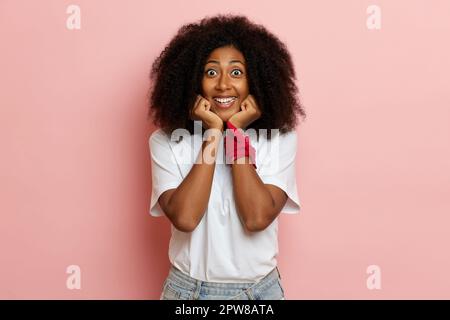 Glückliche afroamerikanische Frau, hält die Hände unter dem Kinn und lächelt. Hochwertiges Foto Stockfoto