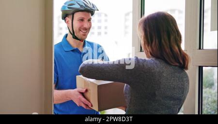 Glückliche junge Frau annehmen Paket Box von Delivery Man Stockfoto