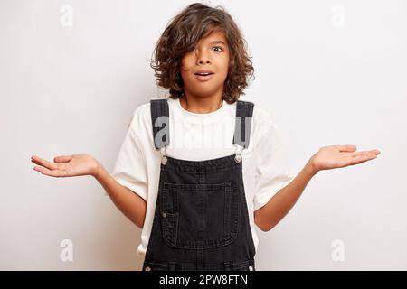Peinlicher, lockiger Teenager mit offenem Mund, die Palmen beiseite, fühlt sich verwirrt und kann keine Entscheidung treffen, isoliert neben der weißen Wand. Hoch Stockfoto