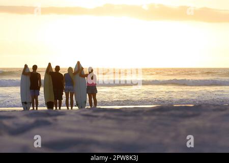 Surfergruppe, Silhouette und Strand mit Platz für Modelle im Urlaub für Freiheit, Jugend oder Natur. Menschen, Frauen und Männer draußen am Meer, Sonnenuntergang und Stockfoto