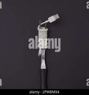 Eine Gabel mit einem USB-Kabel, umwickelt wie Spaghetti auf schwarzem Hintergrund. Minimaler Lebensstil. Stockfoto