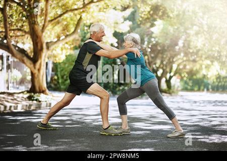 Sich gegenseitig auf dem Weg nach unten in der Fitness unterstützen. Ein Seniorenpaar, das sich vor dem Laufen aufwärmt. Stockfoto