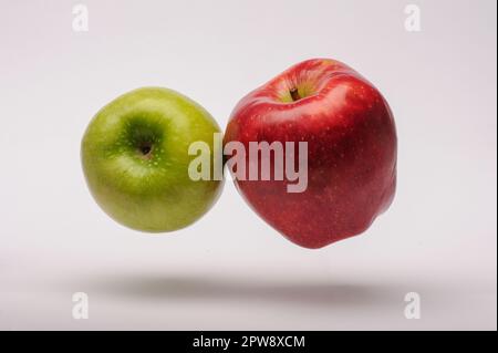 Roter und grüner Apfel, der in der Luft vor weißem Hintergrund hängt Stockfoto