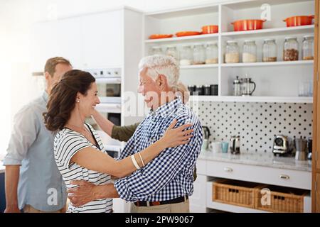 Danke für Ihren Besuch. Eine liebevolle Familie, die sich in der Küche zu Hause mit Umarmungen begrüßt. Stockfoto