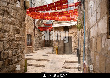 Jerusalem, Israel - 28. April 2023: Enge Straße Jerusalems mit den roten Flaggen des syrisch-orthodoxen Patriarchats Stockfoto