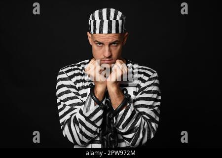 Gefangener in gestreifter Uniform mit angeketteten Händen auf schwarzem Hintergrund Stockfoto