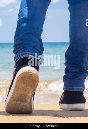 Eine Person, die mit Schuhen am Strand spaziert Stockfoto