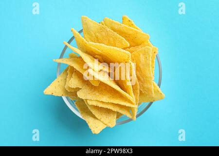 Tortilla-Chips (Nachos) in Glasschüssel auf hellblauem Hintergrund, Draufsicht Stockfoto