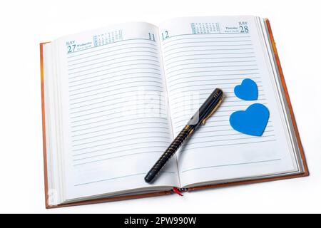 Valentinstagskonzept. Notizbuch mit kleinem blauen Herz und Stift auf weißem Hintergrund. Stockfoto