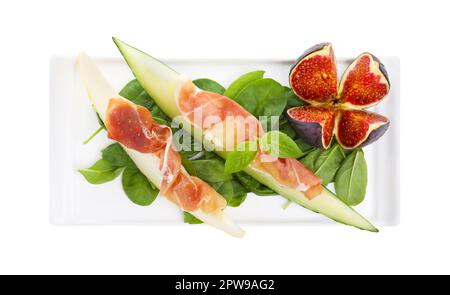 Teller mit leckerer Melone, Jamon, Feigen und Spinat isoliert auf weiß, Draufsicht Stockfoto