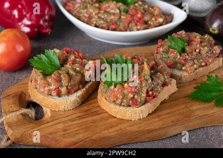 Hausgemachter Auberginen-Kaviar mit Pfeffer, Tomaten und Knoblauch auf Brottoast auf Holzbrett Stockfoto