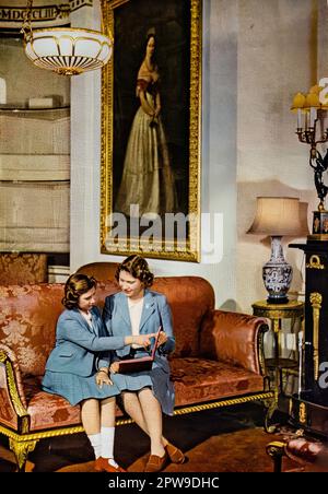 Die 16-jährige Prinzessin Elizabeth, die zukünftige Königin und ihre 11year-jährige Schwester Prinzessin Margaret, sahen hier ein Buch diskutieren, das 1942 in einem speziell in Auftrag gegebenen Farbfoto zum hundertjährigen Bestehen der illustrierten London News fotografiert wurde. Stockfoto