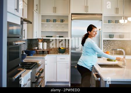 Nach einer sauberen und grünen Diät. Eine schwangere Frau wäscht Gemüse in der Spüle. Stockfoto