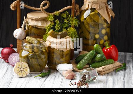 Eingelegte Gurken in einem Glas, frische Gurken, rotes und grünes Chili, Dill, Knoblauch auf Holzhintergrund. Paprika, Zwiebeln und frische Cornflakes Stockfoto