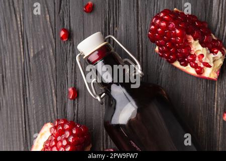 Reifer Granatapfel, verstreute große Körner, frisch gepresster Granatapfelsaft in einer transparenten Flasche auf einem hölzernen Hintergrund von oben. Stockfoto