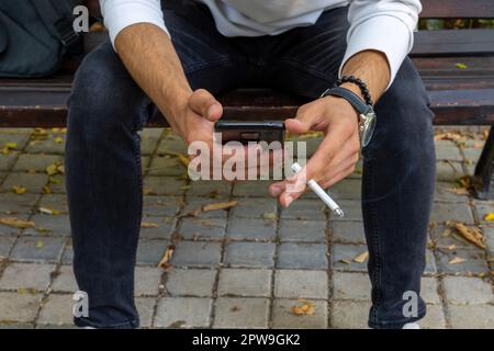 Junger Mann, der eine Zigarette raucht, Telefon in der Hand Stockfoto