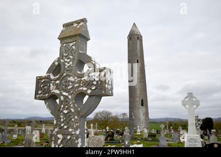 keltische Kreuzung auf dem Friedhof des Klosters Kilmacduagh mit rundem Turm im Hintergrund Grafschaft galway republik irland Stockfoto