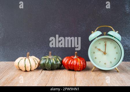 Wecker mit bunten Kürbissen auf Holzboden und schwarzem Holz als Hintergrund. Stockfoto