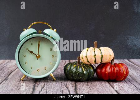 Wecker mit bunten Kürbissen auf Holzboden und schwarzem Holz als Hintergrund. Stockfoto