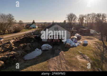 Drohnenfotografie eines Traktors, der im Frühling Heuballen mit Nutztieren in den Schuppen bringt. Stockfoto