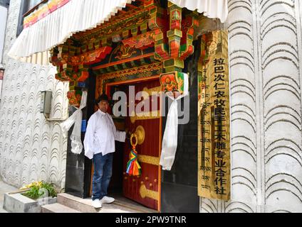 (230429) -- LHASA, 29. April 2023 (Xinhua) -- Lhaba Cering steht am Tor einer professionellen handgefertigten Holzschnitzergenossenschaft für Bauern und Hirten in Lhasa, Hauptstadt der Autonomen Region Tibet im Südwesten Chinas, 25. April 2023. Lhaba Cering, 55, hat große Begeisterung und Liebe für Holzschnitzereien. Im Jahr 1983 nahm Lhaba Cering, damals Lehrling einer Kunsthandwerks- und Architekturfirma in Lhasa, an der routinemäßigen Instandhaltung der Nebengebäude des Potala-Palastes Teil. Seitdem hat sich eine unauflösliche Verbindung zwischen ihm und der Holzschnitzerei gebildet. Die tibetische Holzschnitzerei hat dich Stockfoto