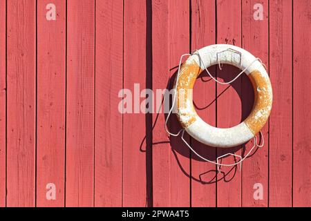 Altes weißes und orangefarbenes Rettungskleid, das an einer roten Holzwand hängt. Stockfoto