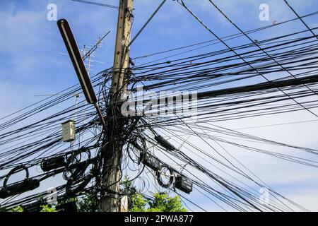 Verhedderte Bündel von Überkopfdrähten. Elektrizitätssystem auf den Straßen Thailands. Kabelgewirr an überlasteten Versorgungsmasten in Thailand. Stockfoto