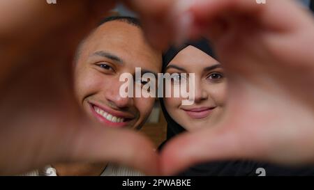 Frisch verheiratete, ethnisch gemischte Ehepaare, afroamerikanischer Mann, mit geliebter arabischer Frau, die durch den Herzrahmen in die Kamera schaut, vereint Ehemann Ehefrau Stockfoto