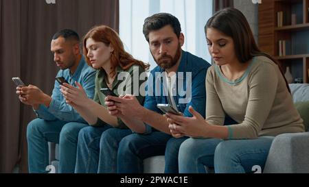 Trauriger Mann, schau dir Freunde an, Handy-süchtig, multiethnische Menschen, die sich in Gadgets verirrt haben, übermäßig nutzen soziale Netzwerke, um online zu chatten, verschiedene langweilige Frauen Stockfoto
