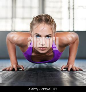 Jammern ist für die Schwachen, Frau oben. Eine sportliche junge Frau, die Liegestütze im Fitnessstudio macht. Stockfoto