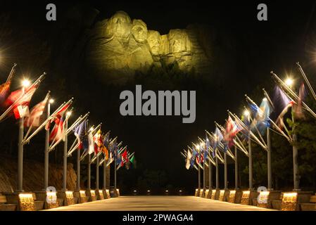 Die Gesichter der Präsidenten auf dem Mount Rushmore scheinen in der Nacht über der beleuchteten Avenue of Flags zu schweben Stockfoto