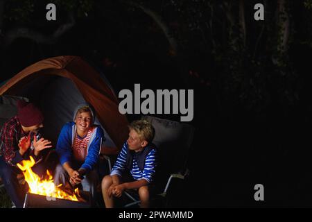 Kameradschaft am Lagerfeuer. Drei junge Jungs, die am Lagerfeuer sitzen. Stockfoto