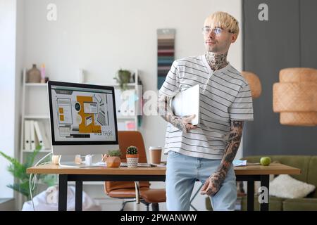 Tätowierter Grafikdesigner mit Laptop im Büro Stockfoto