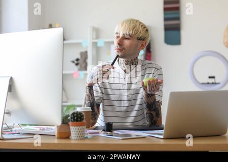 Tätowierter Grafikdesigner mit Apfel, der im Büro am Tisch arbeitet Stockfoto