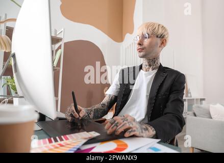 Tätowierter Grafikdesigner, der im Büro am Tisch arbeitet Stockfoto