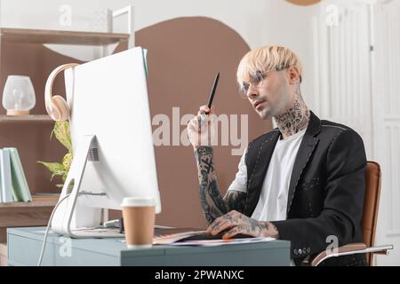 Tätowierter Grafikdesigner, der im Büro am Tisch arbeitet Stockfoto
