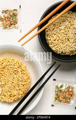 Rohe Instantnudeln in Schüsseln mit Stäbchen und Gewürzen auf weißem Grunge-Hintergrund Stockfoto
