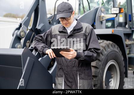 Servicemitarbeiter mit digitalem Tablet am Traktorhintergrund. Hochwertiges Foto Stockfoto