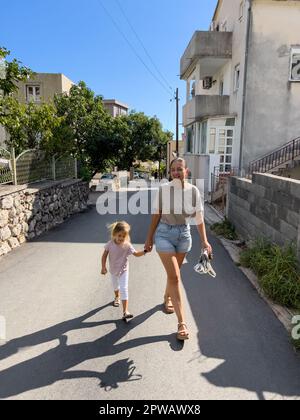 Mom und ein kleines Mädchen gehen Händchen halten auf der Straße einer Kleinstadt Stockfoto