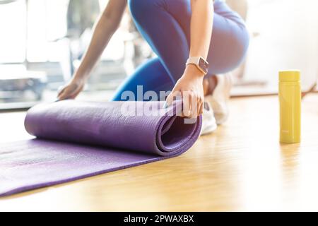 Yogamatte. Closeup Frauen Hände Rollen TPE-Gummi Fitness Yoga Matte auf dem Boden im Sportverein. Stockfoto