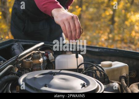 Ein Mann überprüft den Ölstand im Automotor. Selbstbedienung des Autos. Regelmäßige Überprüfung des Ölstands im Motor. Stockfoto